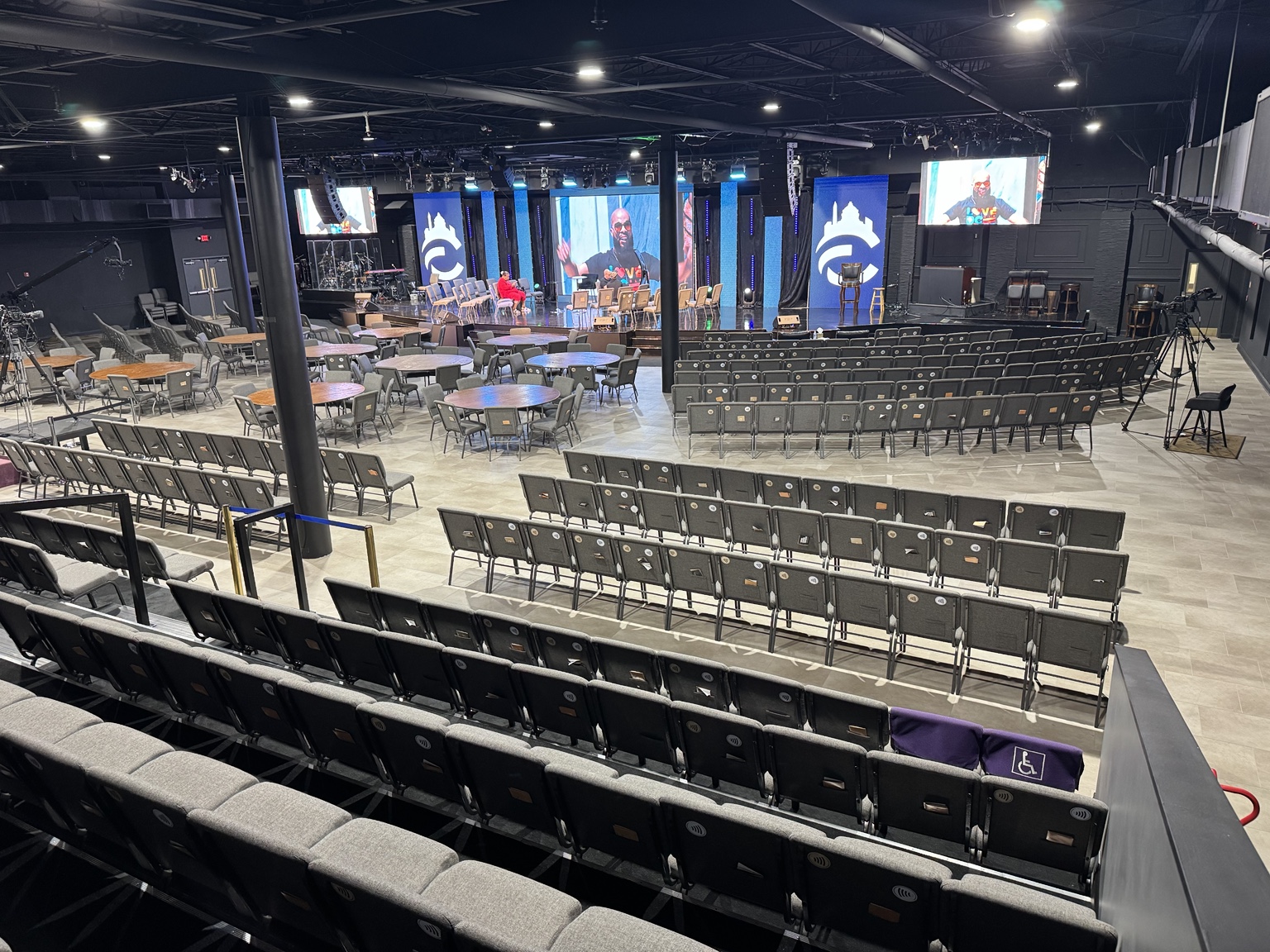 Wide view of the Temple Hills campus venue from the back left, showing the stage, screens, seating, and tables