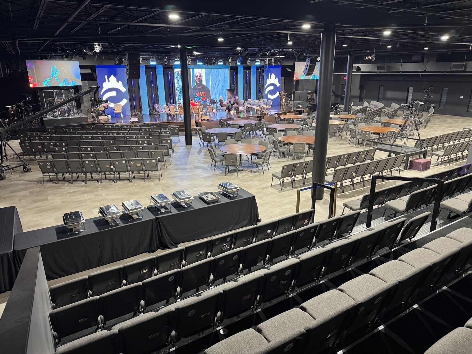 Wide view of the Temple Hills campus venue from the back right, showing the stage, screens, seating, and tables